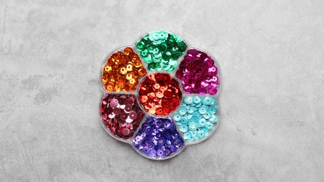 Photo of Many shiny colorful sequins in container on light grey background, top view