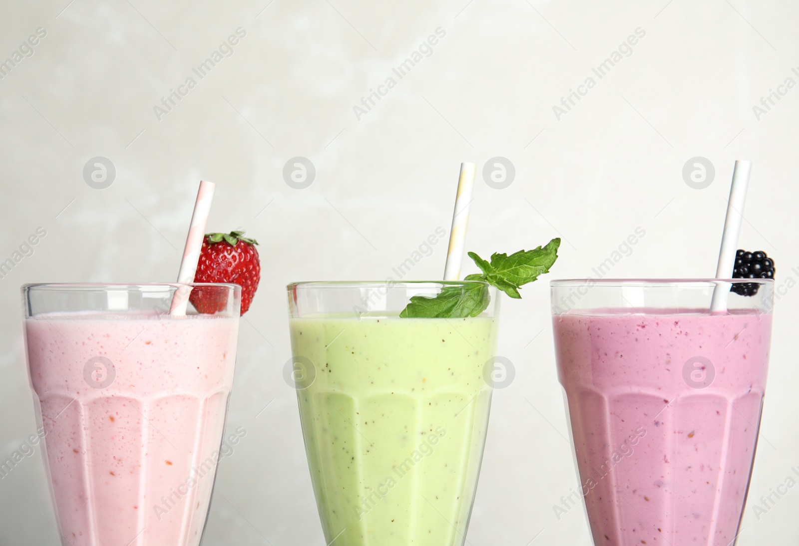 Photo of Tasty milk shakes with fresh berries and mint on light background, closeup