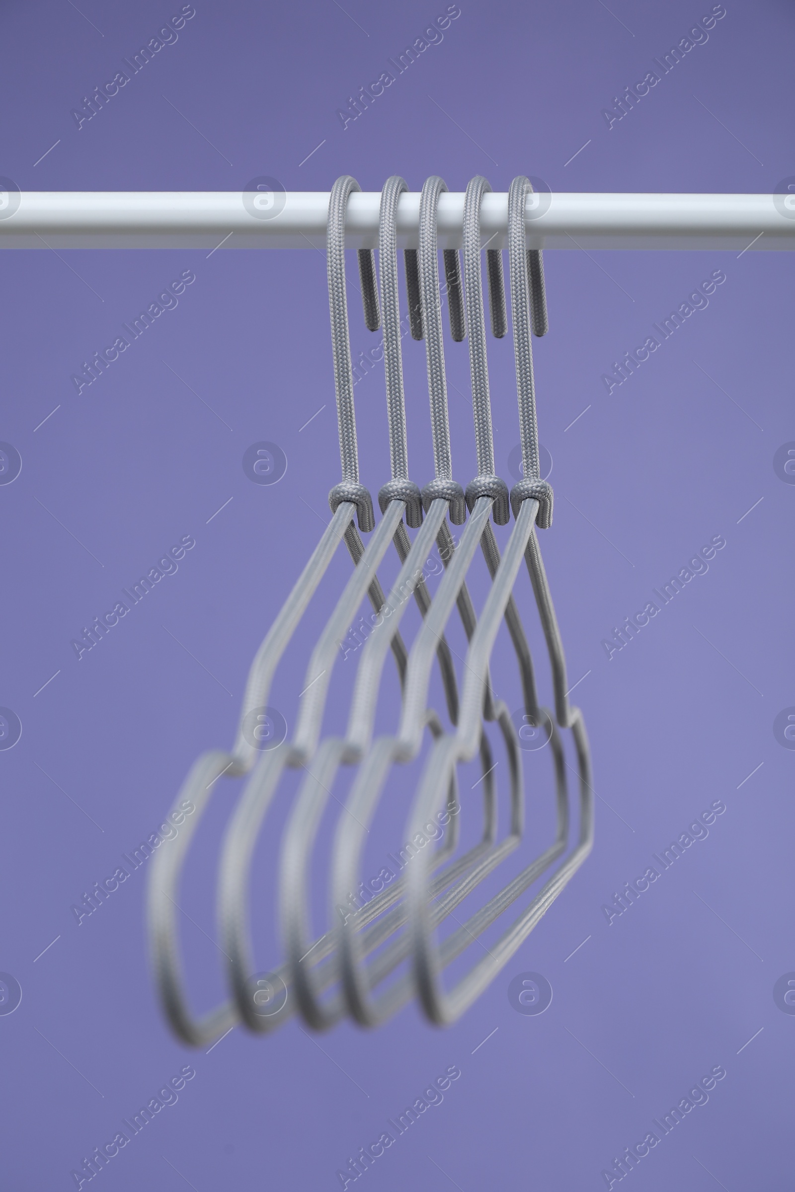 Photo of Empty clothes hangers on rack against purple background, closeup