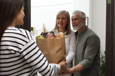 Courier giving paper bag with food products to senior couple indoors