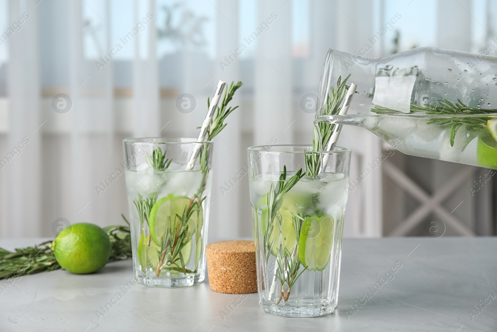 Photo of Pouring tasty refreshing cocktail with rosemary and lime into glass on table