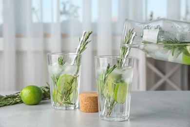 Pouring tasty refreshing cocktail with rosemary and lime into glass on table