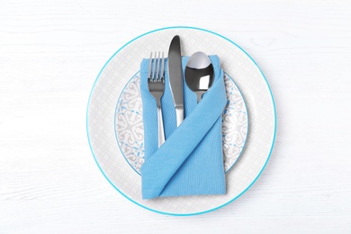 Plates, cutlery and napkin on white wooden background, top view
