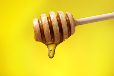 Delicious honey flowing down from dipper against yellow background, closeup