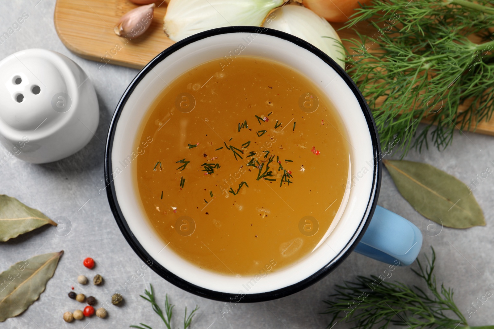 Photo of Hot delicious bouillon in cup and ingredients on light grey table, flat lay