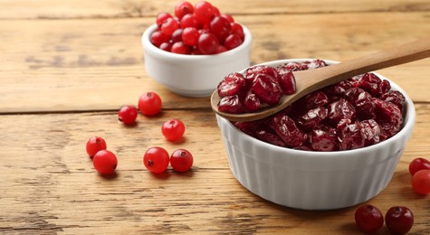 Photo of Tasty dried cranberries in bowl and fresh ones on wooden table, closeup