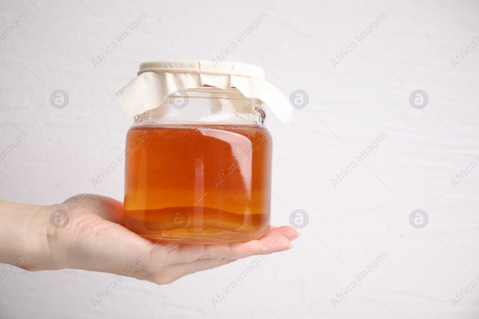 Photo of Woman holding glass jar of tasty kombucha on white background, closeup