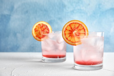 Photo of Glasses of drink with ice cubes and orange on table against color background. Space for text