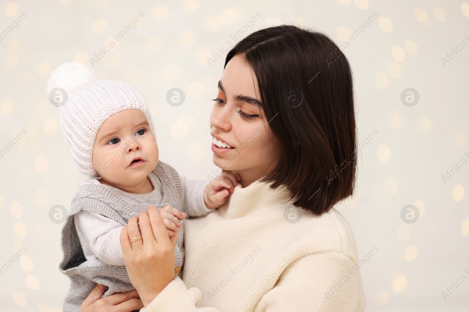 Photo of Happy young mother with her cute baby against blurred festive lights. Winter holiday