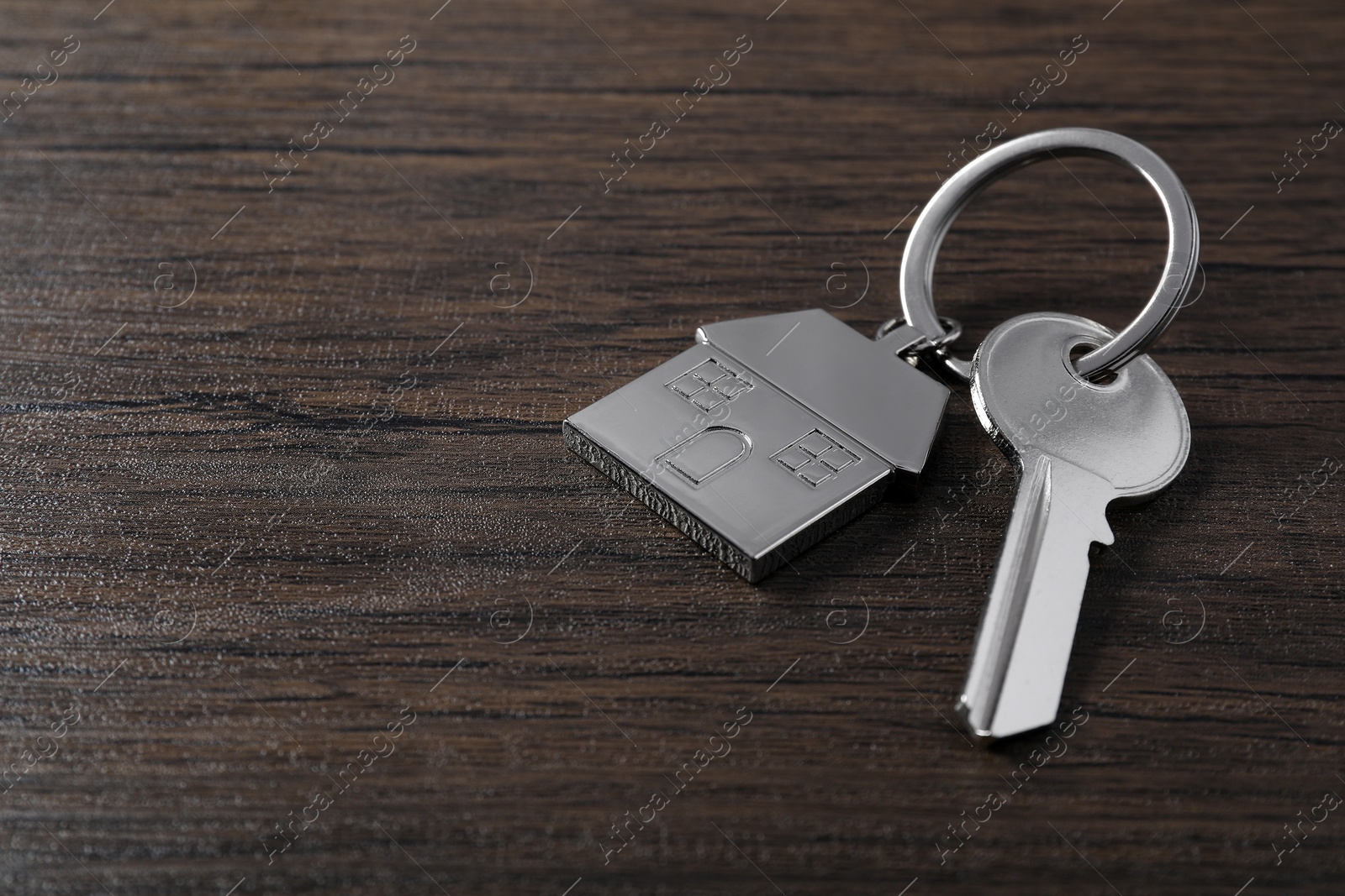 Photo of Key with keychain in shape of house on wooden table, closeup. Space for text