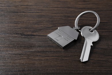 Key with keychain in shape of house on wooden table, closeup. Space for text