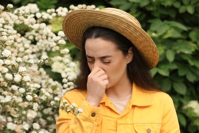 Woman suffering from seasonal pollen allergy near blossoming tree on spring day