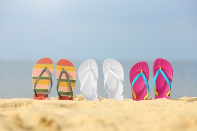 Photo of Different bright flip flops in sand. Beach accessories