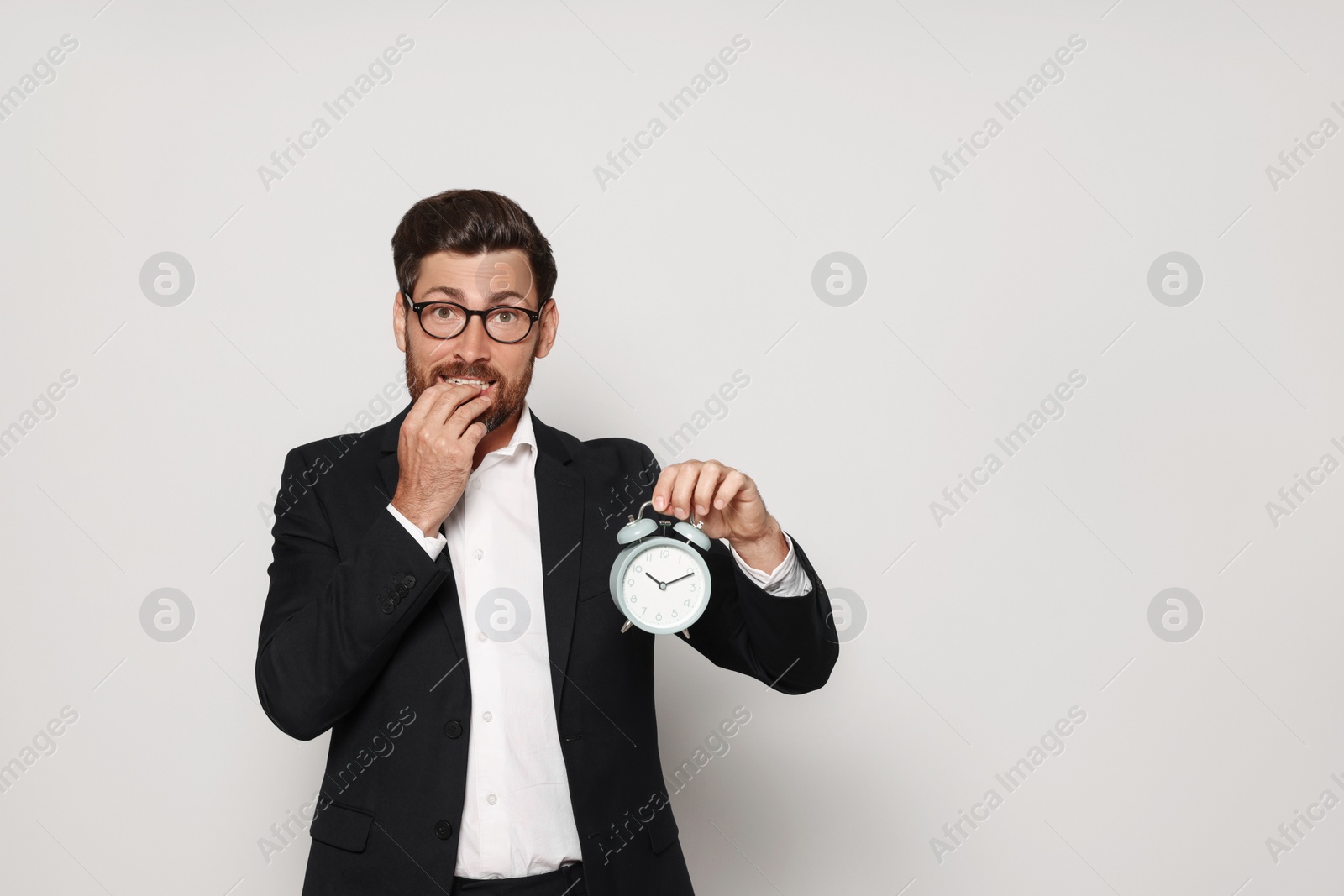 Photo of Emotional bearded man with alarm clock on light grey background, space for text. Being late concept
