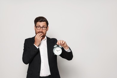 Emotional bearded man with alarm clock on light grey background, space for text. Being late concept