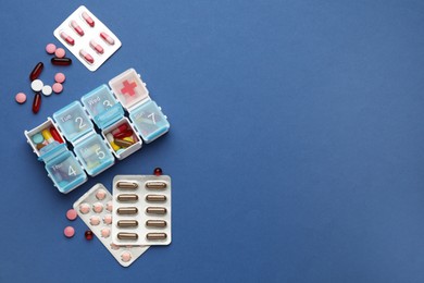 Plastic box with different pills on blue background, flat lay. Space for text