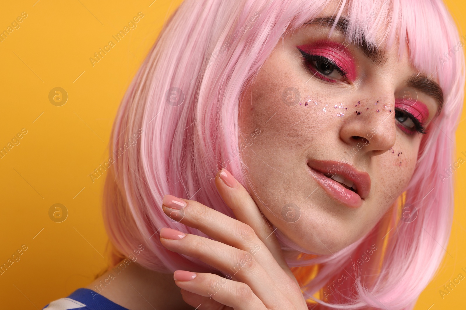 Photo of Beautiful woman with bright makeup and glitter freckles on yellow background, closeup