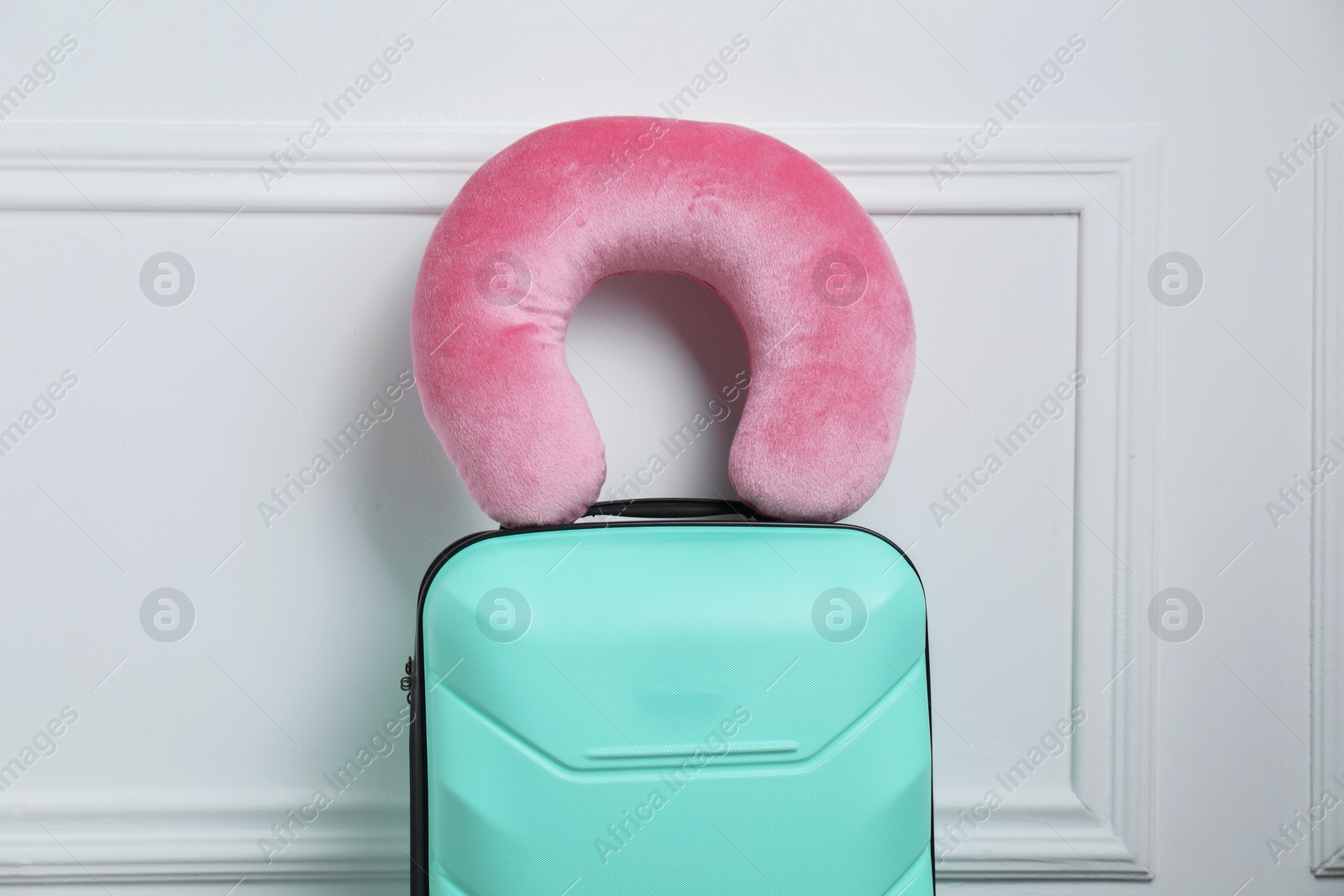 Photo of Pink travel pillow on turquoise suitcase near white wall