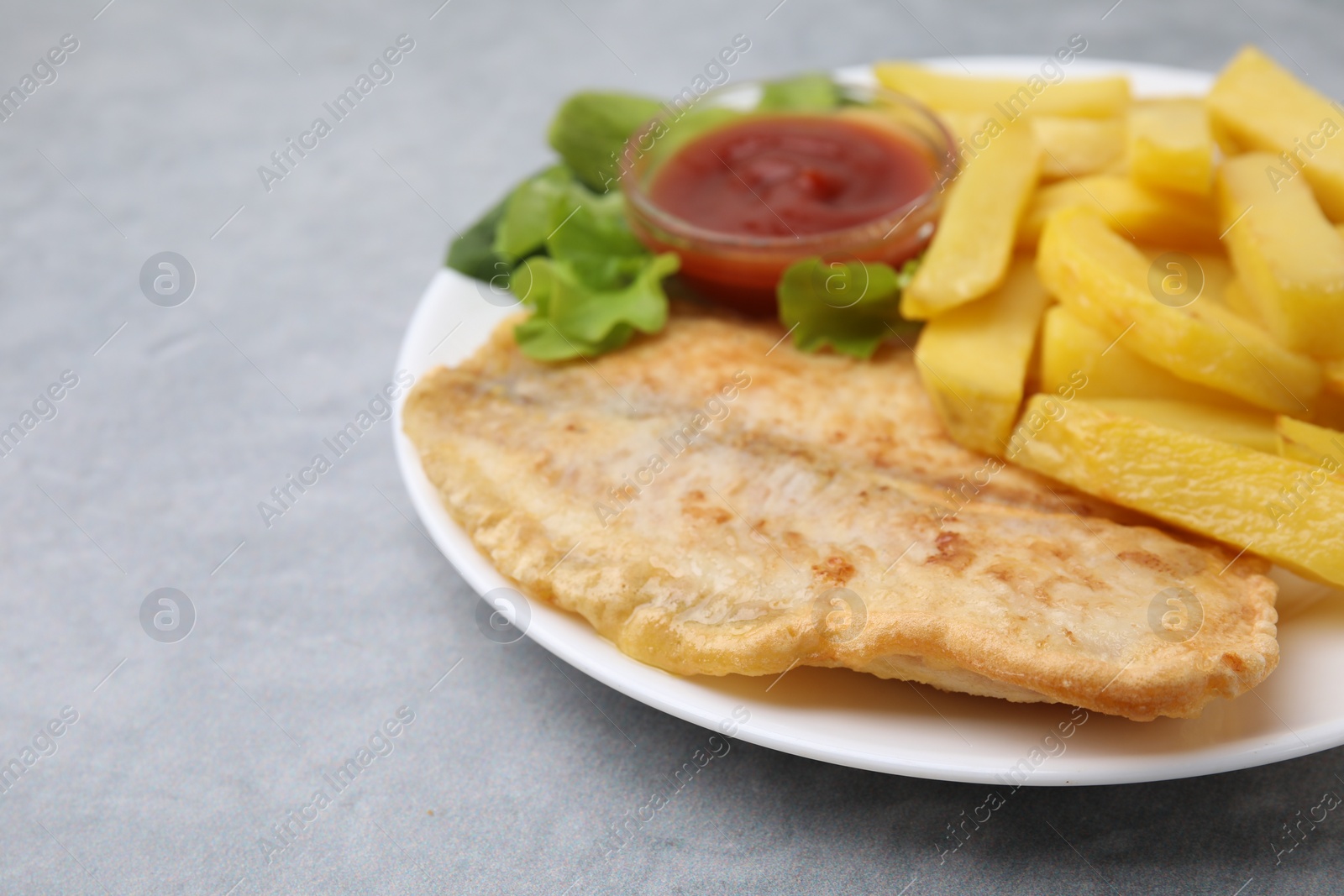 Photo of Delicious fish and chips with ketchup and lettuce on gray table, closeup. Space for text