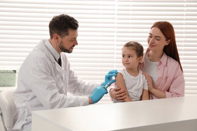 Photo of Children's hepatitis vaccination. Mother with her daughter in clinic. Doctor giving injection to little girl