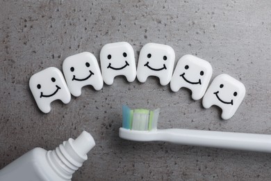 Photo of Plastic teeth with cute faces, toothpaste and brush on grey background, flat lay