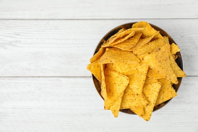 Bowl with tasty Mexican nachos chips on white wooden table, top view. Space for text