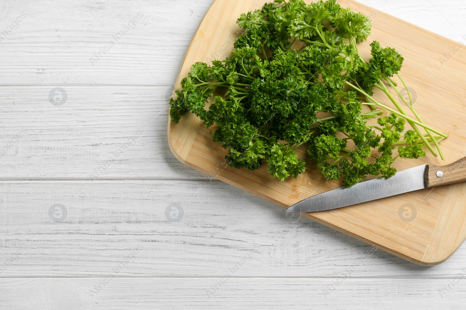 Photo of Fresh curly parsley, cutting board and knife on white wooden table, top view. Space for text