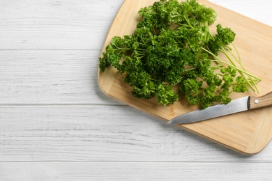 Fresh curly parsley, cutting board and knife on white wooden table, top view. Space for text