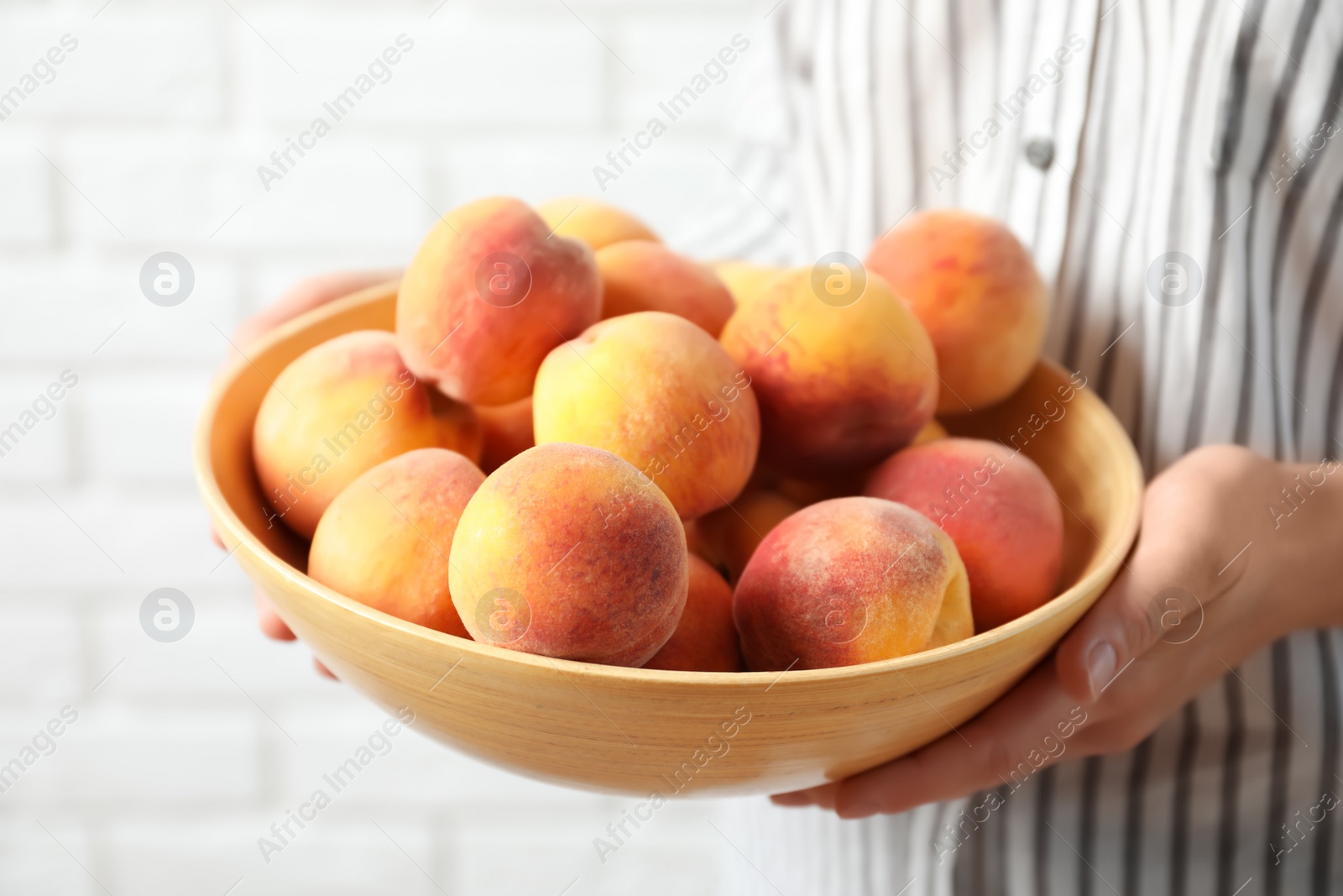 Photo of Woman holding bowl with delicious ripe peaches, closeup