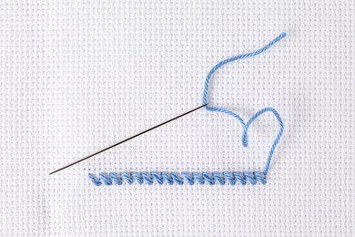 Canvas with embroidery thread and needle, top view