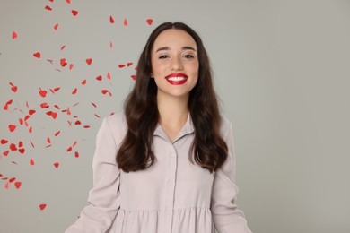 Photo of Beautiful young woman under falling heart shaped confetti on grey background, space for text