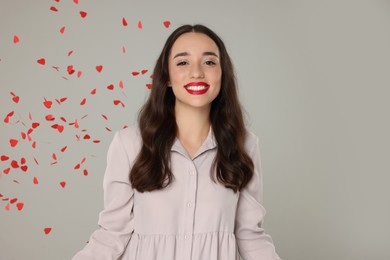 Beautiful young woman under falling heart shaped confetti on grey background, space for text