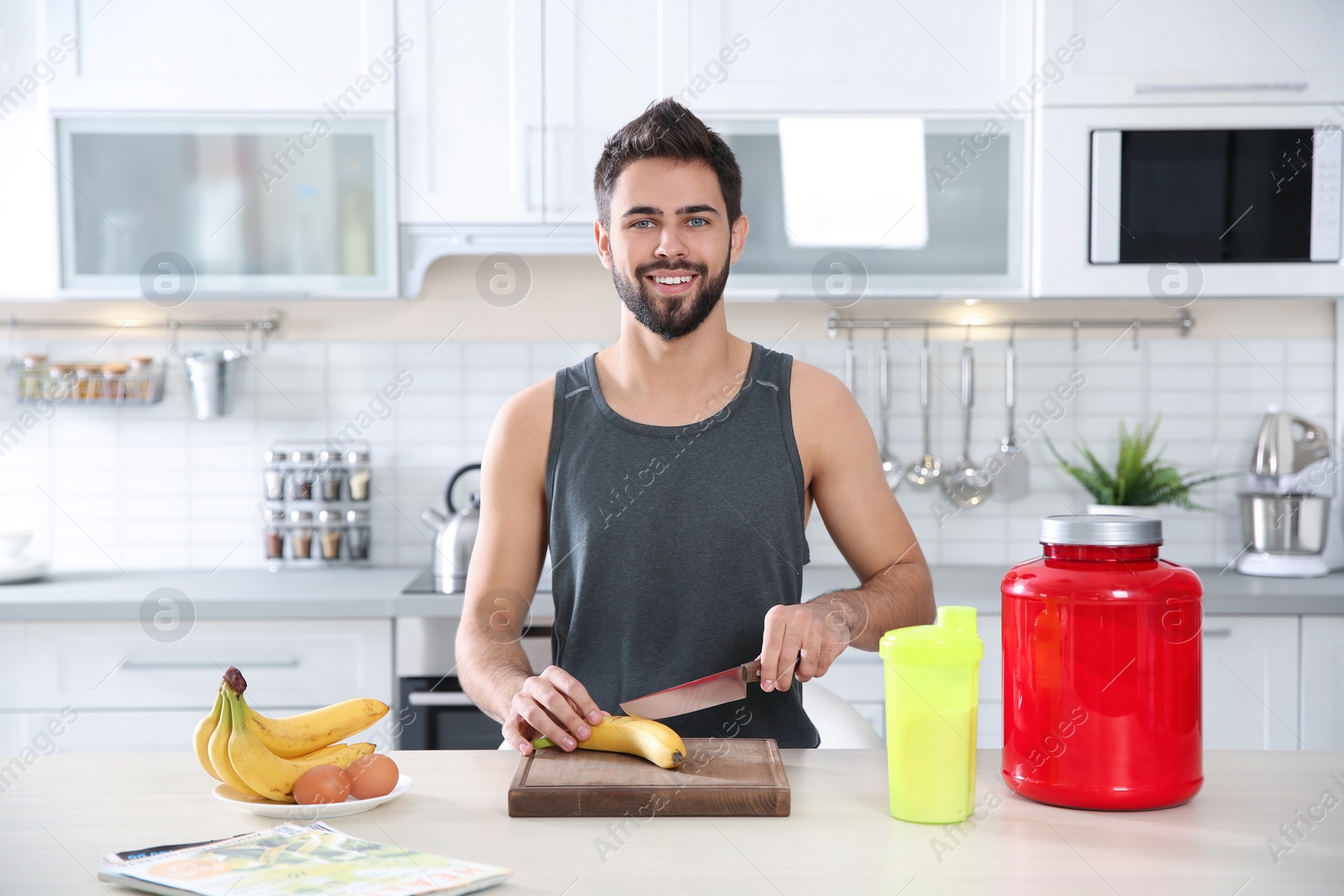 Photo of Young man preparing protein shake at table in kitchen