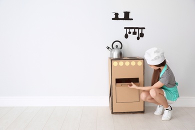 Photo of Little child in chef hat playing with carton stove indoors