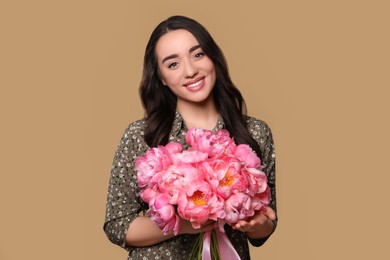 Photo of Beautiful young woman with bouquet of pink peonies on light brown background