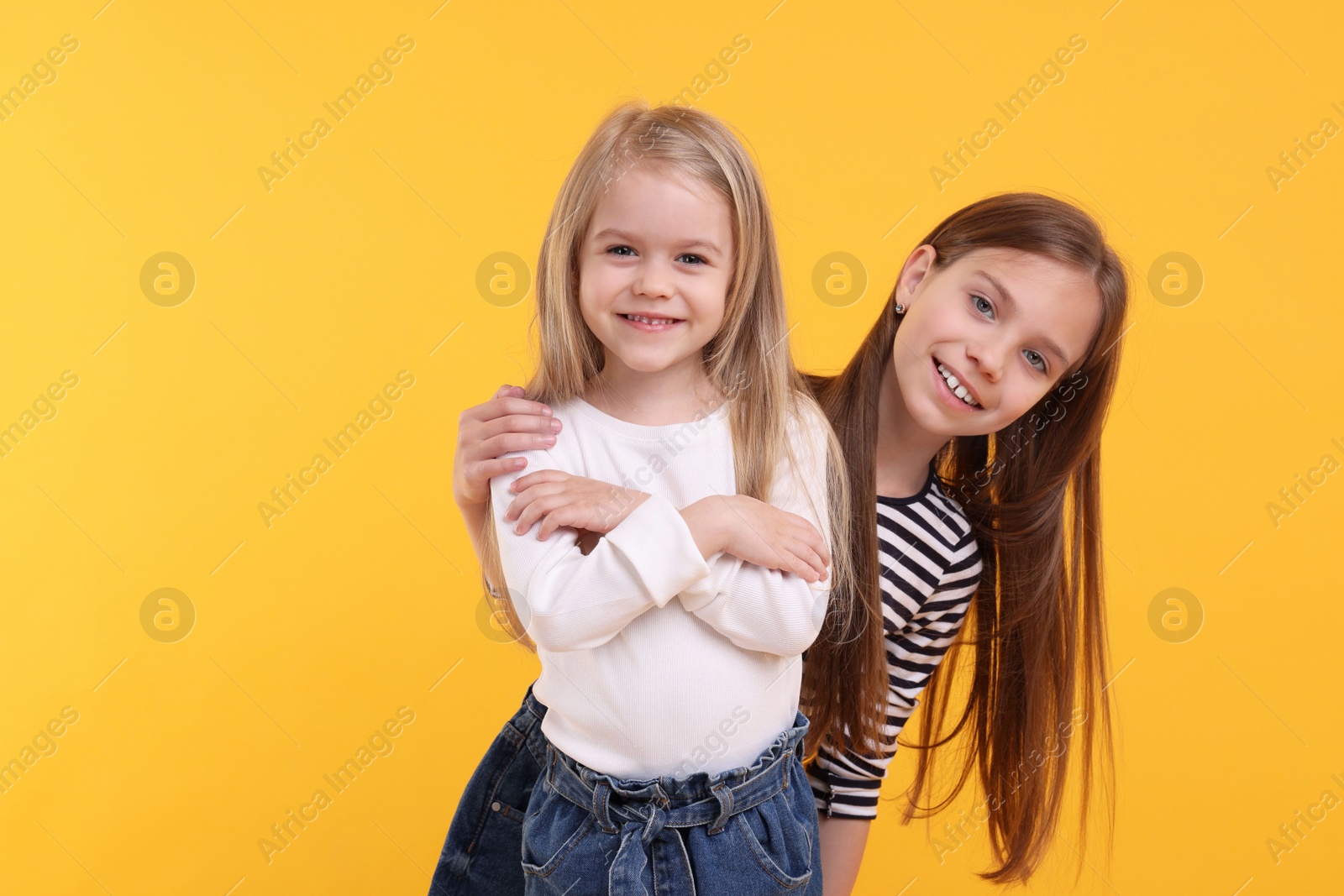 Photo of Portrait of cute little sisters on orange background, space for text