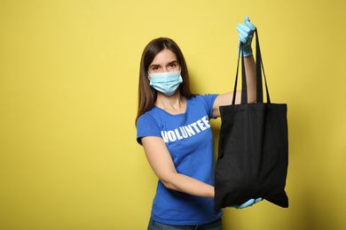 Photo of Female volunteer in protective mask and gloves with black bag on yellow background, space for text. Aid during coronavirus quarantine