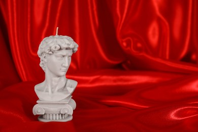Photo of Beautiful David bust candle on red satin. Space for text