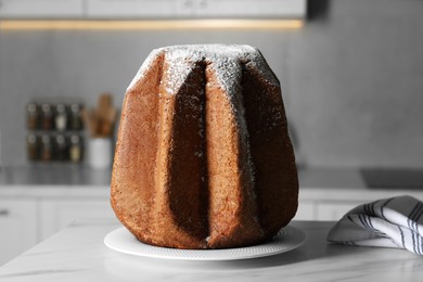 Photo of Delicious Pandoro cake decorated with powdered sugar on white table in kitchen. Traditional Italian pastry