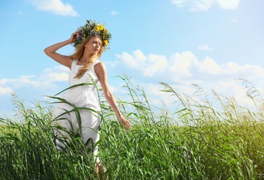 Young woman wearing wreath made of beautiful flowers in field on sunny day