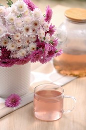 Photo of Fresh delicious herbal tea and beautiful bouquet on wooden table