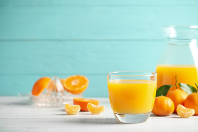 Glass of fresh tangerine juice and fruits on white wooden table. Space for text