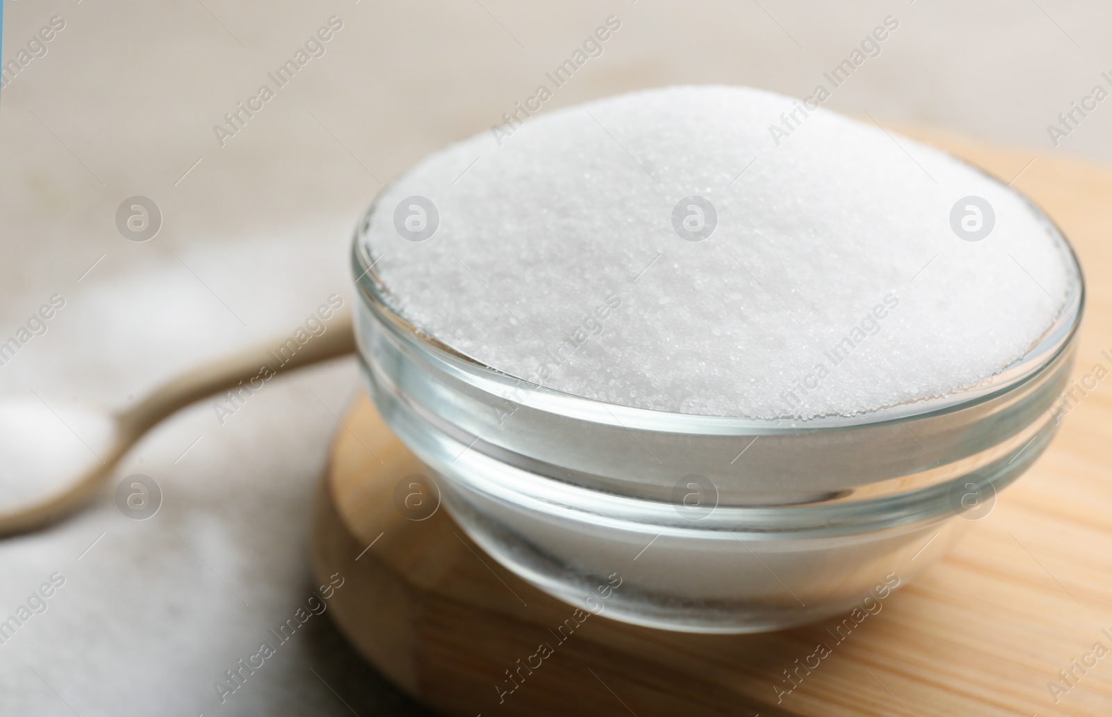 Photo of Glass bowl with salt on wooden board, closeup