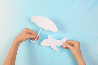 Photo of Woman covering paper plane with umbrella cutout on color background, closeup. Travel insurance concept