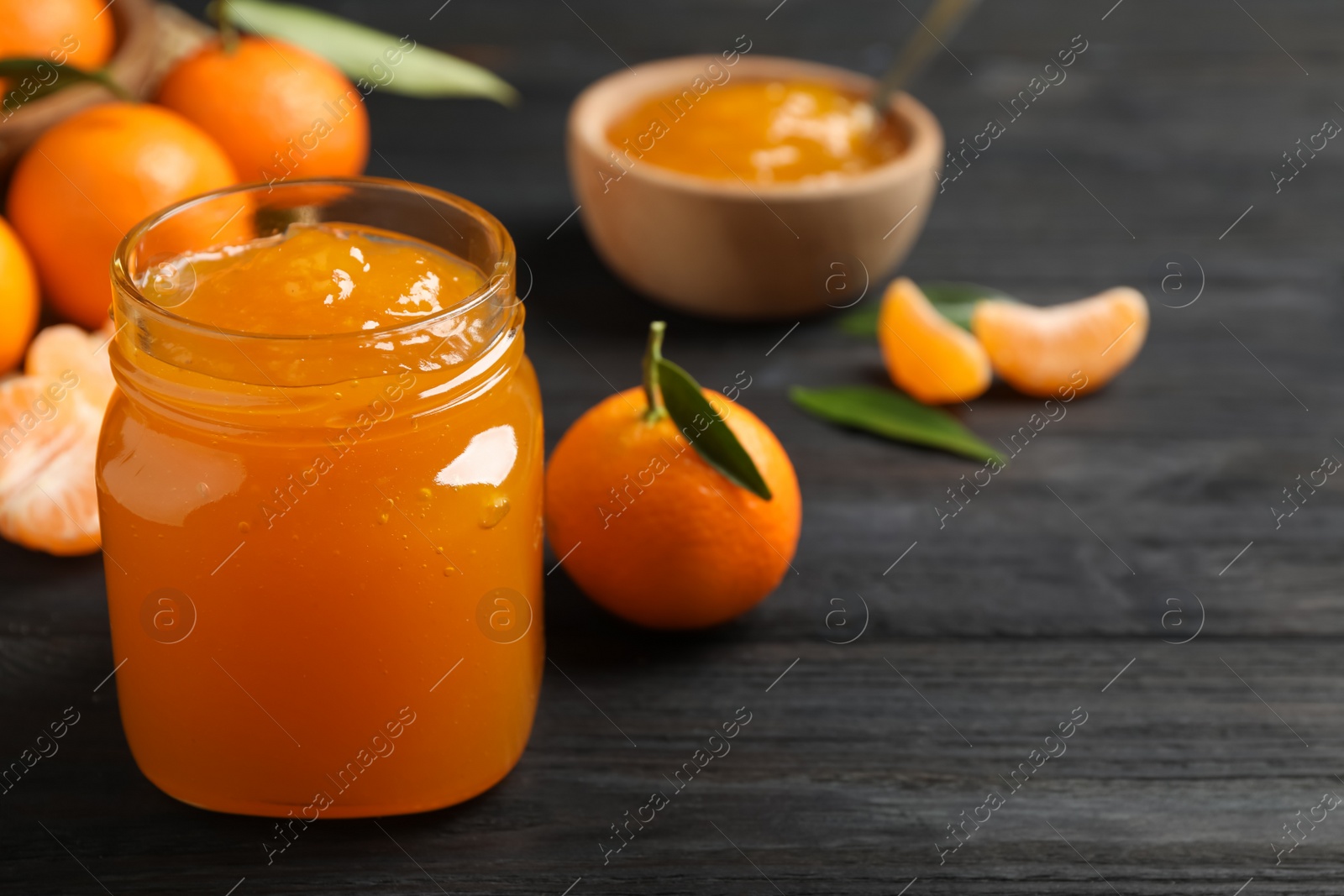 Photo of Tasty tangerine jam in glass jar on dark wooden table. Space for text