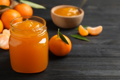 Tasty tangerine jam in glass jar on dark wooden table. Space for text