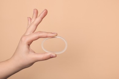 Woman holding diaphragm vaginal contraceptive ring on beige background, closeup. Space for text
