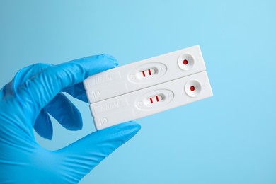 Photo of Doctor holding two disposable express tests for hepatitis on light blue background, closeup