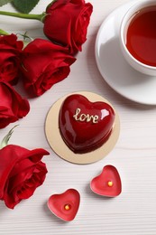 Photo of St. Valentine's Day. Delicious heart shaped cake, tea, roses and candles on white wooden table, flat lay