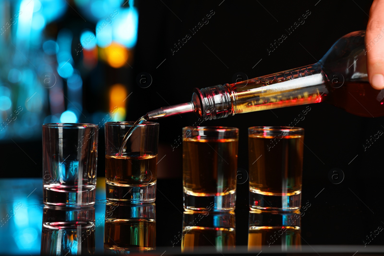 Photo of Pouring alcohol drink from bottle into shot glass at mirror bar counter, closeup